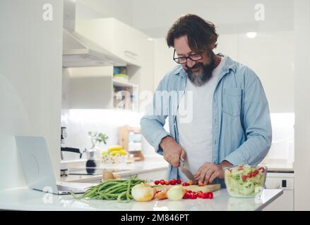 Un seul homme à la maison préparant le déjeuner dans la cuisine. Mode de vie sain personnes coupant des légumes pour préparer une salade légère. Activités de loisirs en intérieur. L Banque D'Images