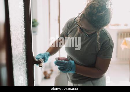 Travail domestique à domicile. Une femme nettoyant la porte de l'appartement avec un spray et des gants. Travail de femme au foyer. Hygiène et aseptisation des lieux de vie. Femme de ménage travaillant un Banque D'Images