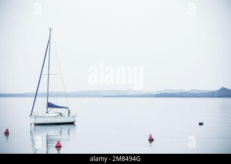 Yacht sur le lac de Garde lors d'une journée de printemps avec des montagnes en arrière-plan. Banque D'Images