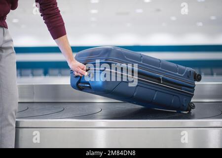 Voyager en avion. Le passager doit récupérer sa valise bleue dans la zone de retrait des bagages du terminal de l'aéroport. Banque D'Images