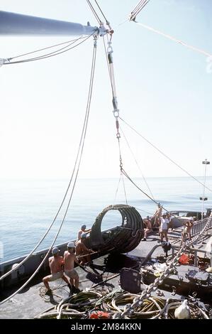 Les membres de l'équipage utilisent une grue pour soulever un morceau d'un moteur de fusée à bord du navire de récupération USS PRESERVER (ARS-8) pendant l'opération de récupération de l'orbiteur de la navette spatiale Challenger. Pays: Océan Atlantique (AOC) Banque D'Images