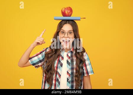 Retour à l'école. Adolescente avec pomme sur la tête, prête à apprendre. Les écoliers sur fond jaune isolé. Banque D'Images