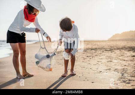 une mère et son fils collectent des bouteilles en plastique sur le bord de mer au coucher du soleil. ils les ont mis dans un sac écologique. concept d'écologie et de soin de la planète Banque D'Images