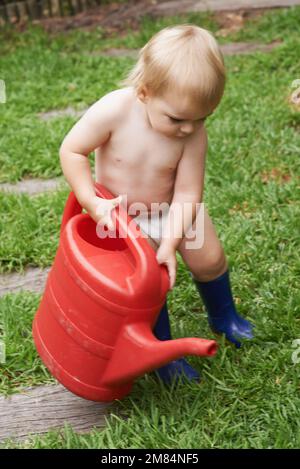 Curieux de savoir comment fonctionne la nature. Un adorable petit garçon qui abreuvoir le jardin. Banque D'Images