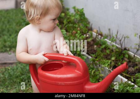 Curieux de savoir comment fonctionne la nature. Un adorable petit garçon qui abreuvoir le jardin. Banque D'Images