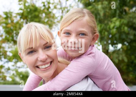 Comme la mère comme la fille. Une jeune mère heureuse donnant à sa fille une promenade en pigeyback dans le parc. Banque D'Images