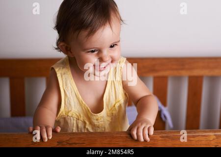 Elle apprécie ses nouvelles compétences. Une adorable petite fille riant alors qu'elle se tient debout dans son berceau. Banque D'Images