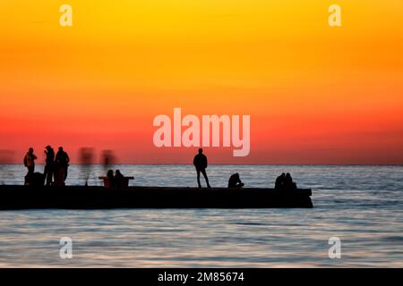 Silhouette de gens regardant le coucher du soleil sur le Molo Audace dans le vieux port de Trieste, Italie Banque D'Images