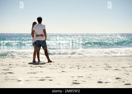 En admirant la vue. Une vue arrière d'un couple qui regarde l'océan sur la plage. Banque D'Images