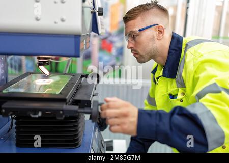 Ingénieur assis dans la salle de fabrication du robot utiliser la machine de mesure de microscope vérifier micropuce Banque D'Images