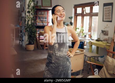 Artiste femme, poterie et téléphone dans l'atelier avec le sourire, la conception et le foyer pour les petites entreprises. Entrepreneur d'art asiatique, conversation et smartphone Banque D'Images