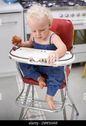 Je peux me nourrir moi-même. Un petit bébé heureux mangeant de la nourriture solide tout en étant assis sur une chaise haute. Banque D'Images