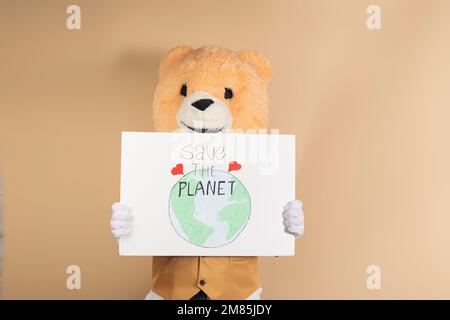 Homme portant un masque d'ours en peluche sur un fond jaune, tenant un panneau en carton qui dit: 'Save the Planet'. Concept de prendre soin de la planète et du glob Banque D'Images