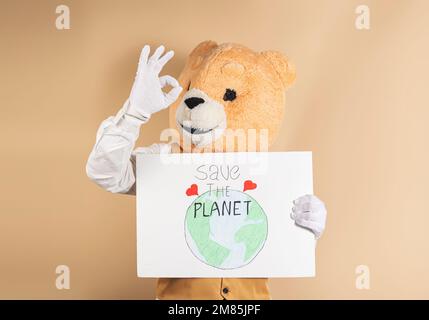 Ours en peluche avec un corps humain qui montre OK tout en tenant un panneau qui dit "Save the Planet". Banque D'Images