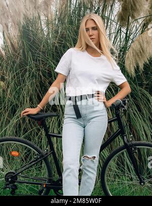 Jeune belle fille pose dans un t-shirt blanc à côté de son vélo. Maquette verticale. Banque D'Images