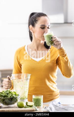 Une jeune femme aime un smoothie aux épinards qu'elle s'est faite elle-même. Elle boit une boisson énergétique végétale. Banque D'Images