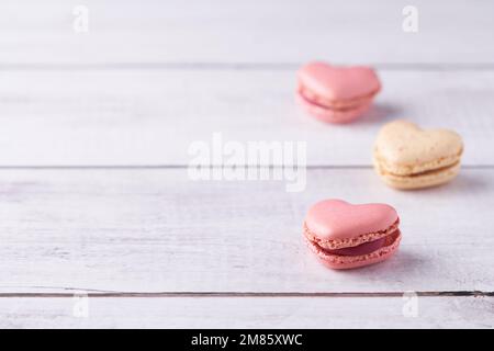 Trois macarons français en forme de coeur, remplis de crème sur fond de bois blanc. Confiserie traditionnelle pour la Saint-Valentin, la fête des mères ou le mariage. Banque D'Images