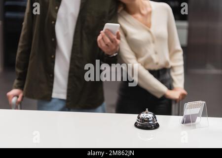 cloche de service et porte-carte sur le bureau de réception près d'un couple court avec smartphone sur fond flou, image de stock Banque D'Images