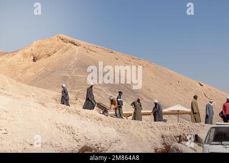 LOUXOR, ÉGYPTE - 27 décembre 2022. Groupe de musulmans arabes locaux travaillant dans le désert creusant le sable dans la montagne sous le ciel bleu Banque D'Images