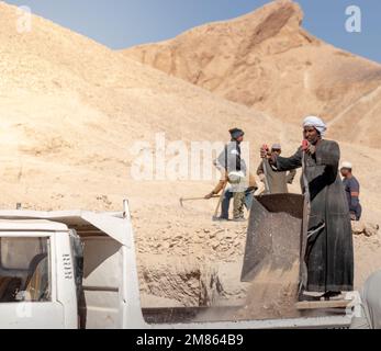 LOUXOR, ÉGYPTE - 27 décembre 2022. Vieil homme arabe égyptien avec turban travaillant dans la montagne avec chariot de travail et sable dans la vallée des rois Banque D'Images