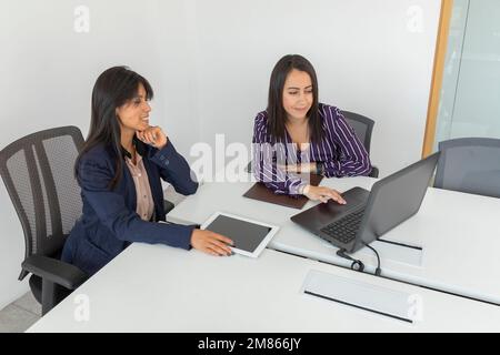 Deux collègues de travail discutent tout en examinant un projet sur leur ordinateur portable. Femmes latines travaillant au bureau. Banque D'Images