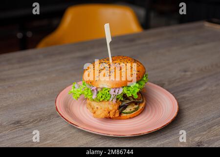 Assiette à gros plan avec hamburger de poulet appétissant juteux isolé sur fond de table en bois. Servir un gros sandwich calorique sur une brochette. Café de restauration rapide Banque D'Images