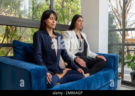 Vue latérale de deux femmes d'affaires méditant sur un fauteuil tout en prenant une pause au travail dans le bureau. Banque D'Images