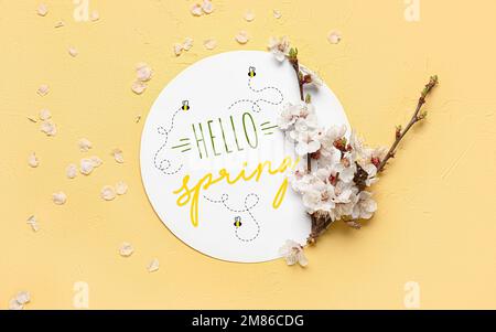 Belles branches de printemps en fleurs et carte avec texte HELLO SPRING sur fond jaune Banque D'Images