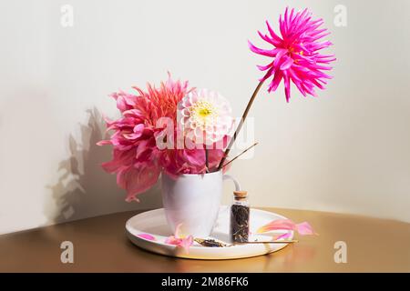 Tasse en porcelaine avec branches roses en fleur de chrysanthèmes sur plateau de service blanc sur fond gris, espace de copie. Herbes sèches parfumées pour le thé Banque D'Images