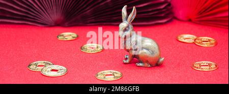 Bannière avec une figure en bronze d'un lapin avec des pièces en or - le symbole du nouvel an chinois 2023 sur fond rouge, espace copie. Banque D'Images