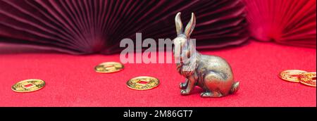 Bannière avec une figure en bronze d'un lapin avec des pièces en or - le symbole du nouvel an chinois 2023 sur fond rouge, espace copie. Banque D'Images