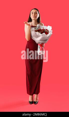 Jeune femme avec bouquet de fleurs soufflant baiser sur fond rouge. Célébration de la Saint-Valentin Banque D'Images