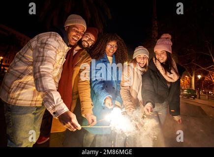 Groupe d'amis célébrant avec des feux d'artifice de sparklers à la fête de nuit. Diverses ethnies Banque D'Images