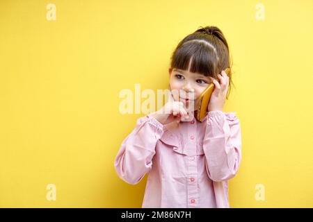 Drôle d'enfant fille de parler au téléphone avec quelqu'un, de penser.Enfant caucasien regardant à côté, concentré dans la pensée. Portrait de l'enfant ayant le tal sérieux Banque D'Images