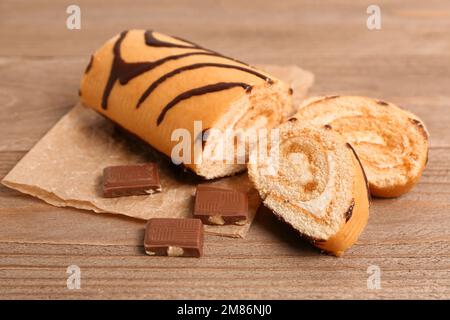 Papier à pâtisserie avec morceaux de délicieux rouleaux de gâteau éponge et chocolat sur table en bois Banque D'Images