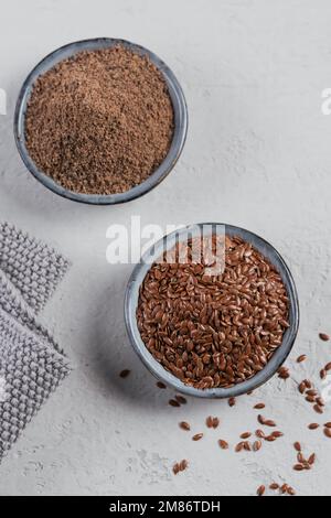 Brunir les graines de lin et les graines de lin ou lin broyées ou broyées dans un petit bol sur fond gris clair. Banque D'Images