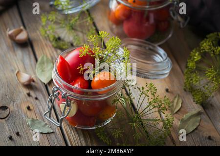 Conserver les tomates fraîches et marinées, les assaisonnements et l'ail sur une table en bois. Aliments fermentés sains. Légumes en conserve à la maison. Banque D'Images