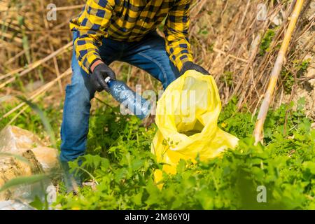 Une personne portant des gants et collectant des plastiques dans une forêt, concept d'écologie Banque D'Images