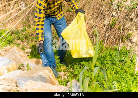 Une personne portant des gants et collectant des plastiques dans une forêt, concept d'écologie Banque D'Images