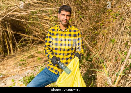 Une personne portant des gants et collectant des plastiques dans une forêt, concept d'écologie Banque D'Images