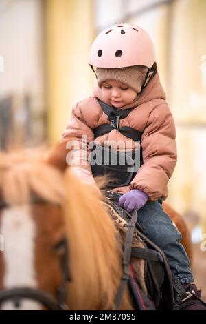 Leçon de équitation pour les petits enfants. Une jeune fille de trois ans fait du poney et fait des exercices Banque D'Images