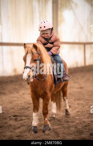 Leçon de équitation pour les petits enfants. Une jeune fille de trois ans fait du poney et fait des exercices Banque D'Images