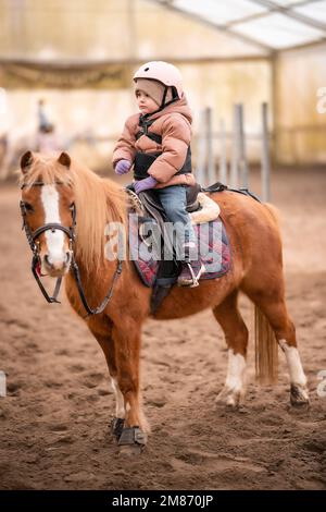 Leçon de équitation pour les petits enfants. Une jeune fille de trois ans fait du poney et fait des exercices Banque D'Images