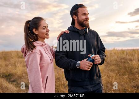 Portrait en plein air d'un couple positif dans la nature campagne se détendre avant ou après le jogging. belle femme et homme à capuche riant, parlant. nous Banque D'Images
