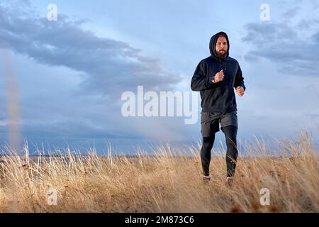 guy jogging sur le terrain portant des vêtements de sport noirs, s'entraîner à courir à l'air frais le matin. le type d'athlète caucasien barbu est motivé, concentré Banque D'Images