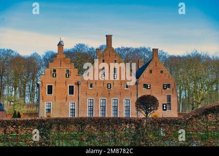 Musée Menkemaborg, Uithuizen, Groningen, pays-Bas, manoir datant de 14-17th-siècle, par une journée ensoleillée. Haie de hêtre en couleurs d'hiver au premier plan Banque D'Images