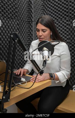 une femme parle dans un microphone tout en enregistrant un podcast, en utilisant une cabine audio avec isolation acoustique. Banque D'Images