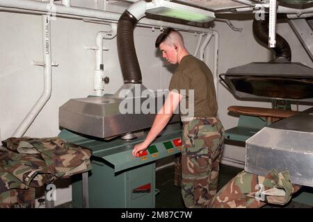 Un membre du détachement de la Marine à bord du porte-avions à propulsion nucléaire USS THEODORE ROOSEVELT (CVN 71) presse des uniformes utilitaires dans la buanderie du navire. Base : USS Theodore Roosevelt (CVN 71) Banque D'Images