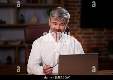 Homme âgé aux cheveux gris travaillant au bureau à domicile avec un ordinateur portable. Portrait d'affaires d'un beau responsable assis sur le lieu de travail. Étudier des cours en ligne Banque D'Images