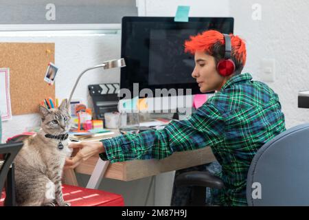 Une jeune femme Latina aux cheveux courts travaille à la maison tout en peetting son chat assis sur son bureau. Banque D'Images